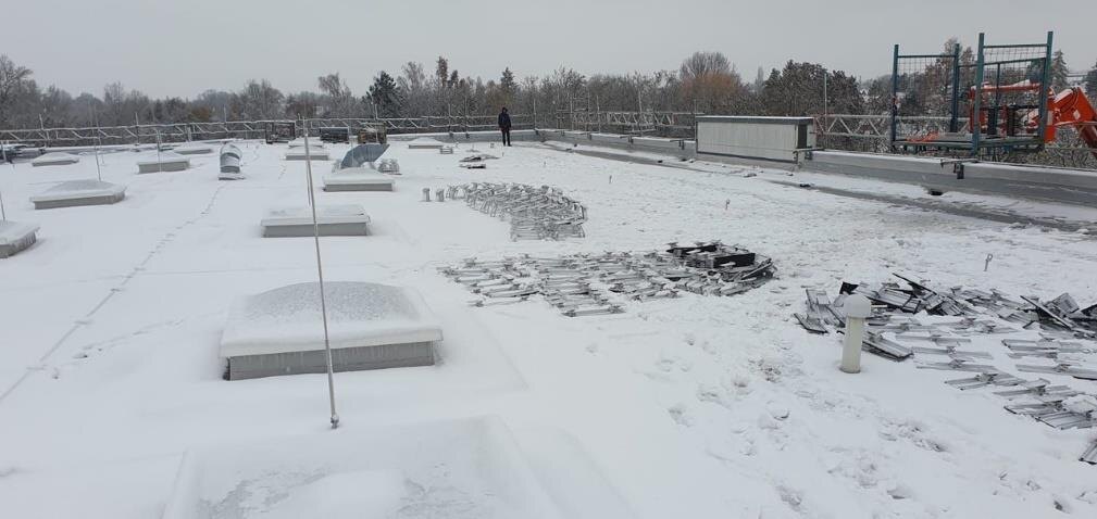 Schneebedecktes Flachdach der Klinik mit Lichtkuppeln während der Montagephase