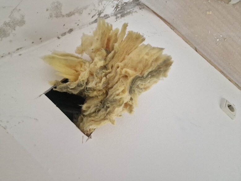 Bauteilöffnung in der Decke einer Dachgeschosswohnung mit heraushängender Dämmwolle